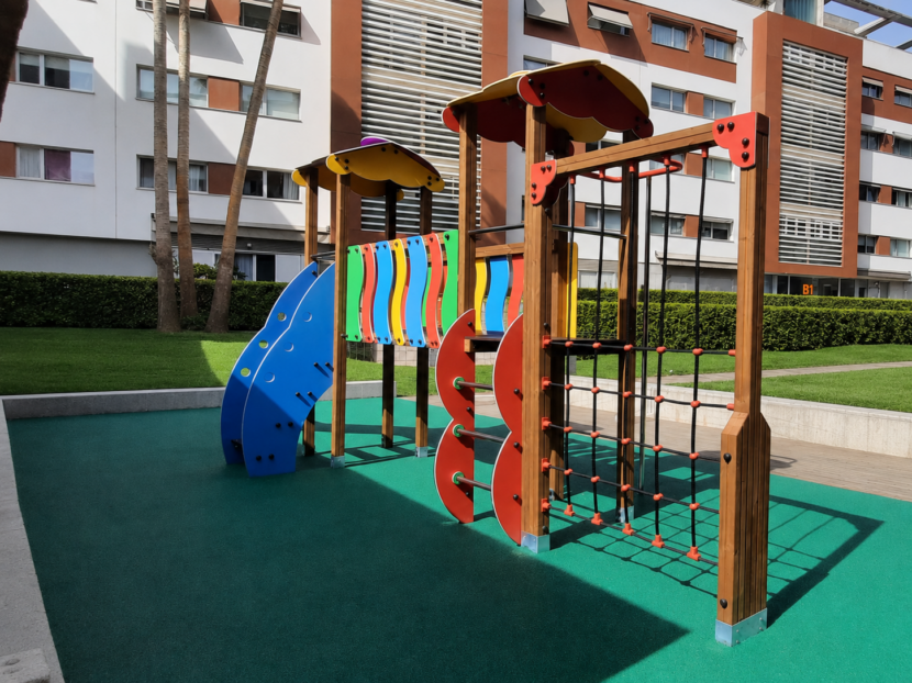 Parque infantil de madera con tobogán, redes de trepa y paneles de colores